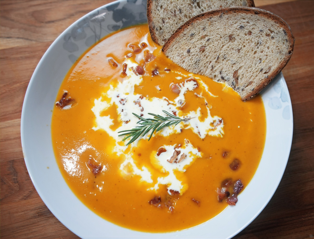 A bowl of butternut squash soup topped with cream, bacon and 7-grain rye bread