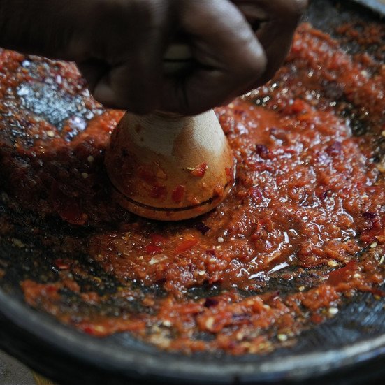 crushing peppers using hand pestle and stone mortar