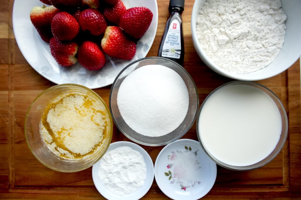 ingredients needed to make a strawberry cobbler; strawberries, flour, vanilla, milk, butter, baking powder, salt