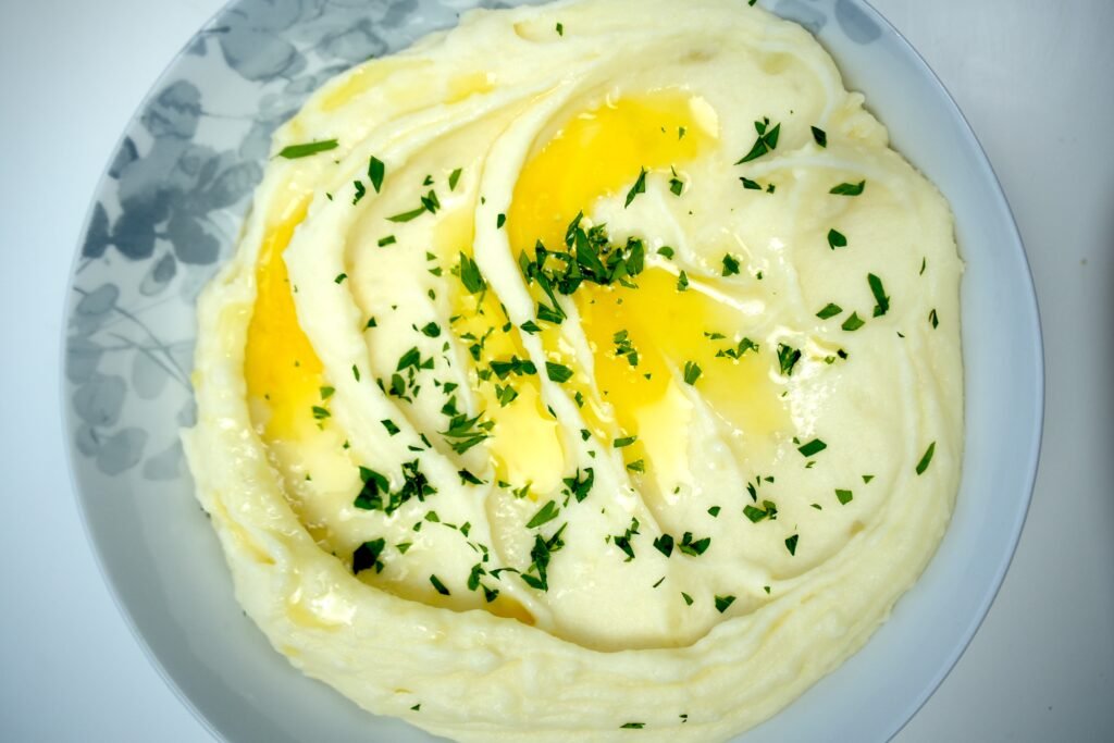 a bowl of buttery mashed potatoes with butter and garnished with chopped parsley